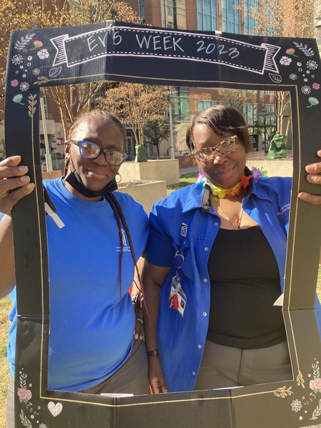 2 EVS staff pose in front of picture frame during block party