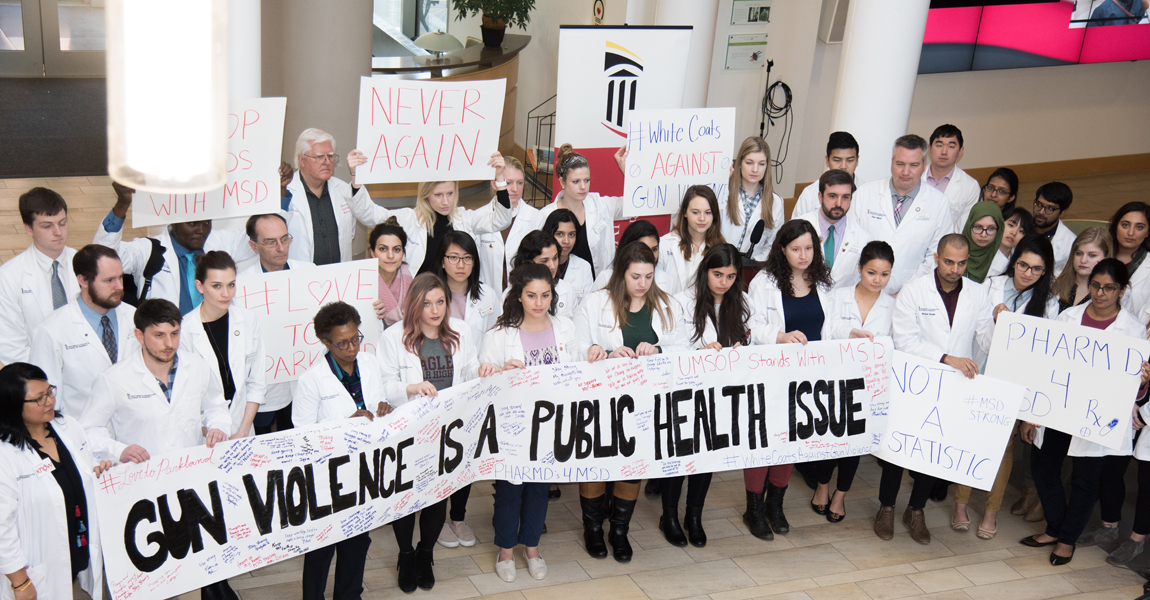 UM School of Pharmacy Dean Natalie Eddington, PhD, FAAPS, FCP, in the front row, third from left, stands next to student Allison Cowett of Parkland, Fla., who wears a green MSD High School shirt beneath a white coat, at a rally against gun violence held in the school's atrium.