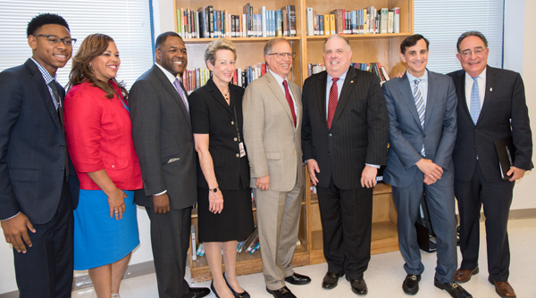 Standing left to right are Brooklyn, NY P-TECH graduate Radcliff Sadler, Maritha Gay of Kaiser Permanente, Baltimore City School Board Chair Marnell Cooper, Acting State Superintendent of Schools Karen Salmon, Stanley Litow of IBM, Governor Larry Hogan, Johns Hopkins President Ronald Daniels, and UMB President Jay Perman.