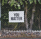 Image of sign behind fence that reads, 