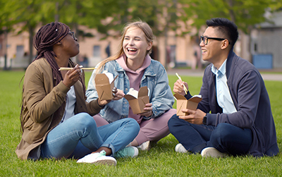 Three students sitting on a lawn and eating