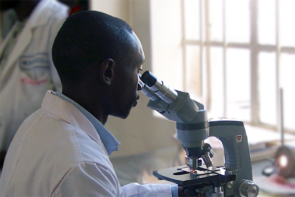 A student clad in a lab coat examining a microscope