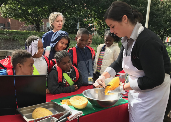 Third-grade students from Robert Coleman Elementary School watch a spaghetti squash cooking demonstration put on by CulinArt at the University Farmers Market.