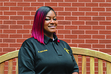 Portrait of Officer Erika Malone in front of bricks while sitting on a light brown bench