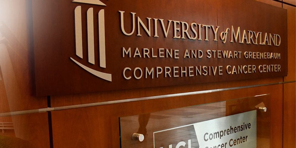 Close-up shot of a wooden sign with the University of Maryland Marlene and Stewart Greenebaum Comprehensive Cancer Center logo engraved on it