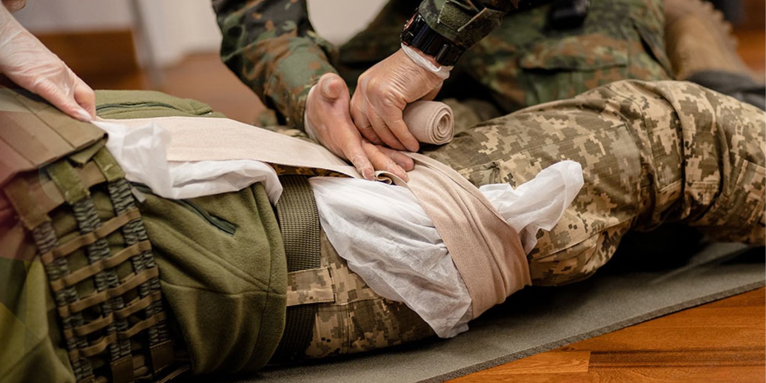 Close-up stock image of a military member's leg receiving trauma care from a health care worker in military clothes