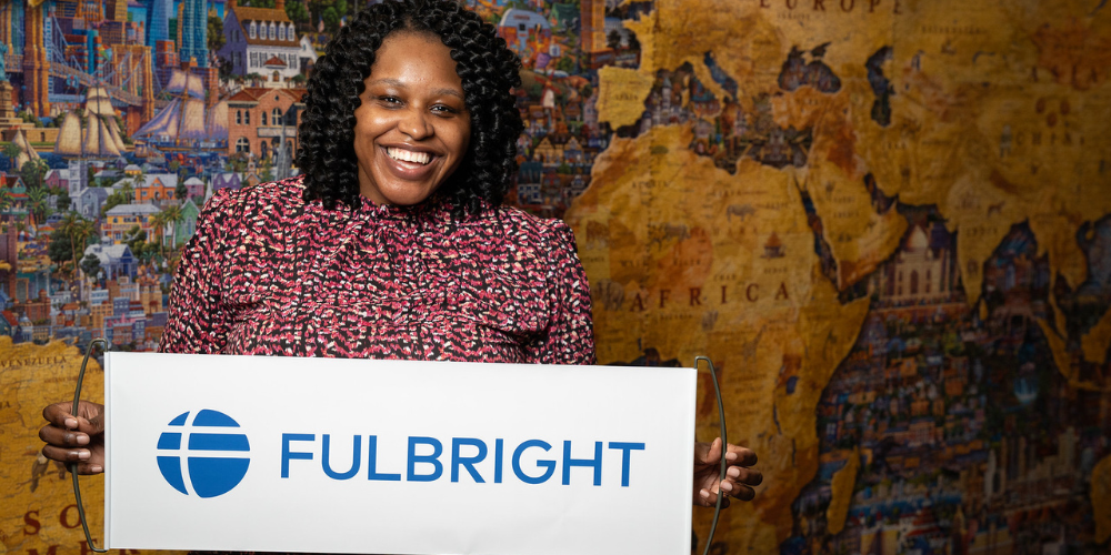 A woman hold a Fulbright banner in front of a large puzzle map