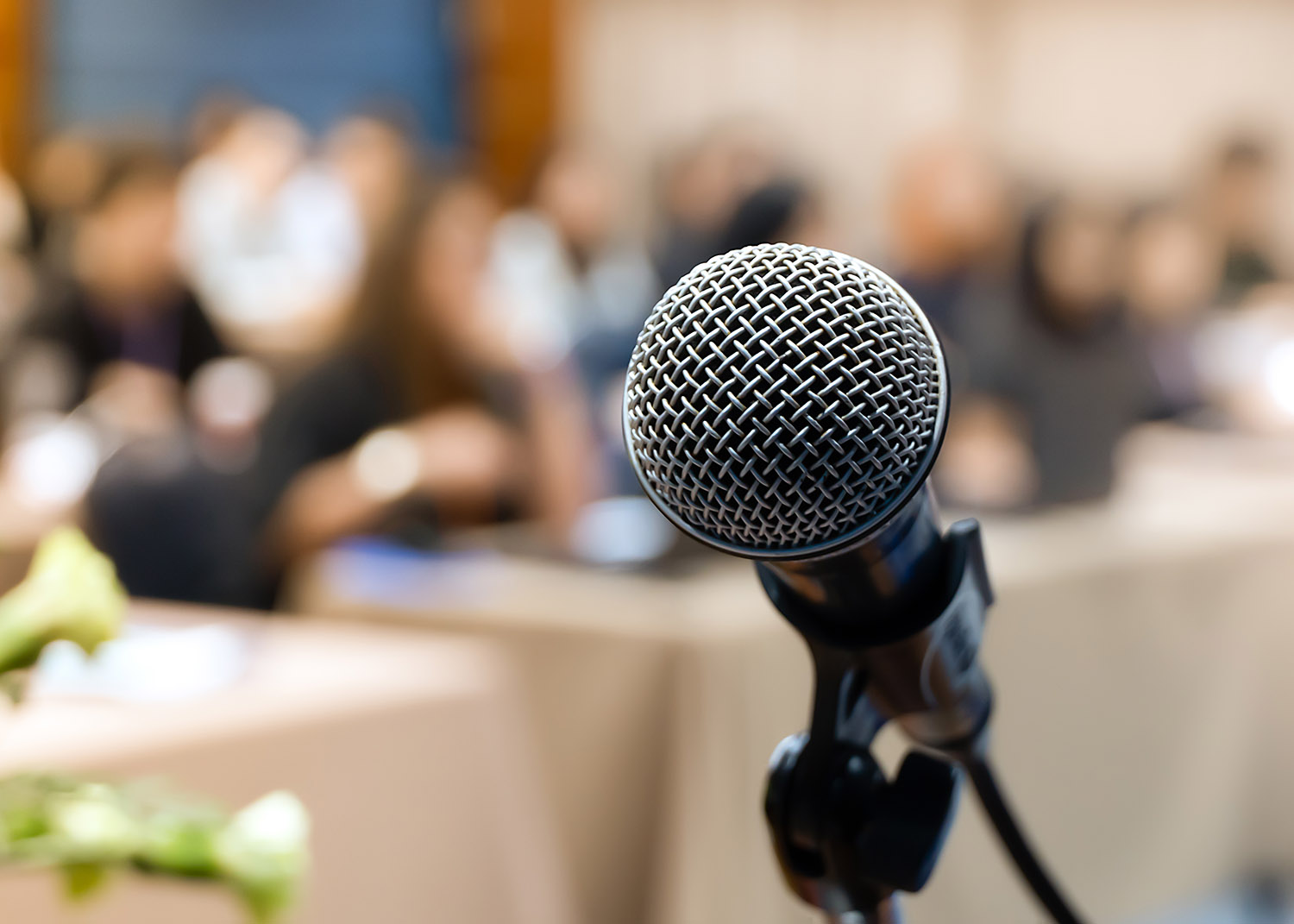 microphone in forefront, people in a meeting hall in the background