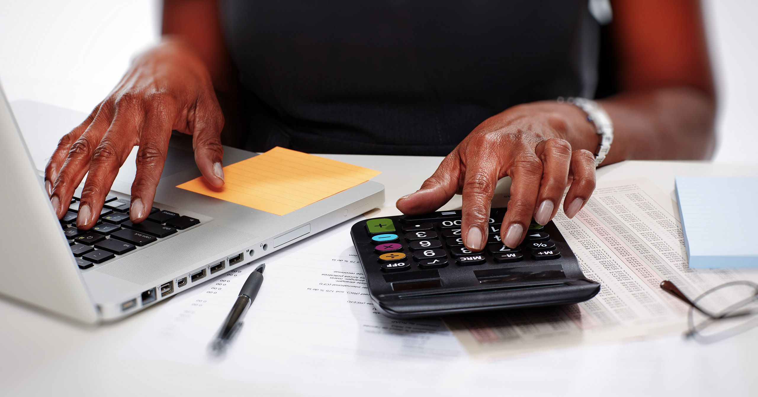 A person uses a calculator and laptop to check financial records