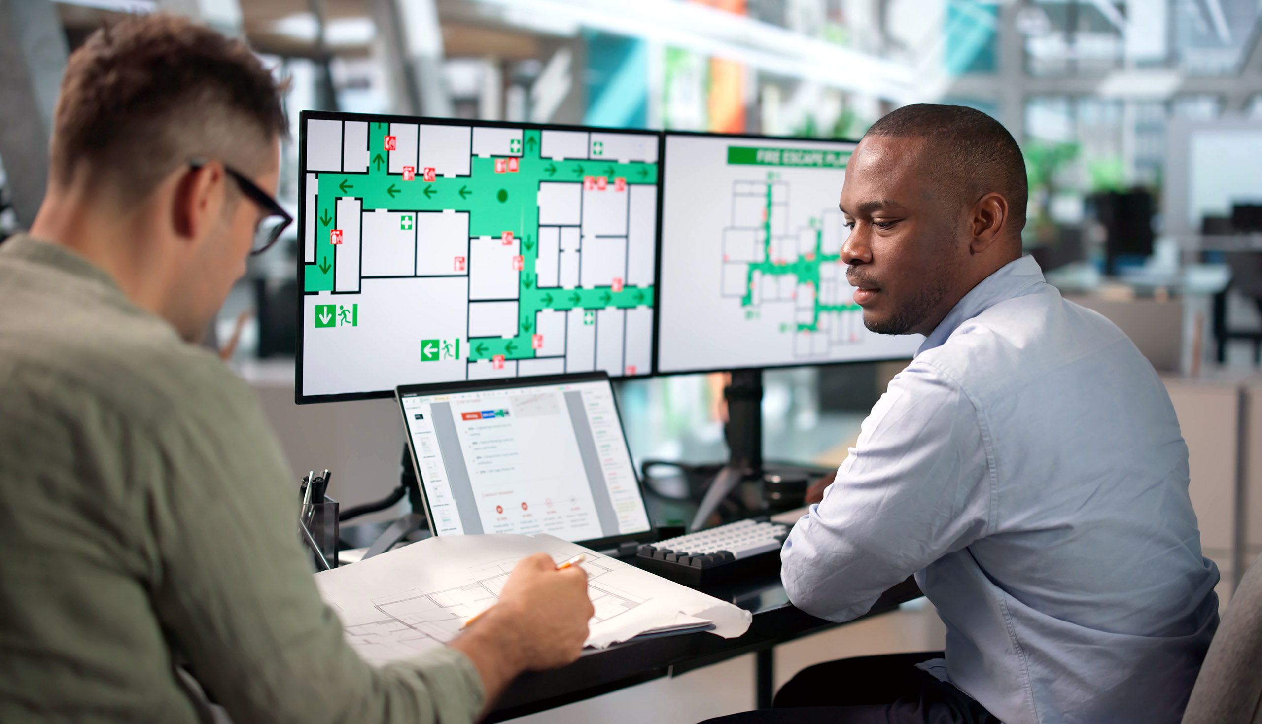 two professionals looking at floorplans on computer screens and paper drawings