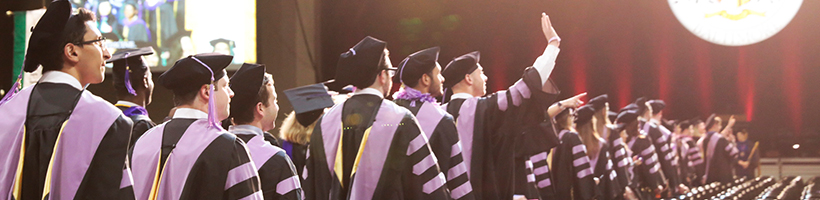 Students in graduation regalia walking down to their seats