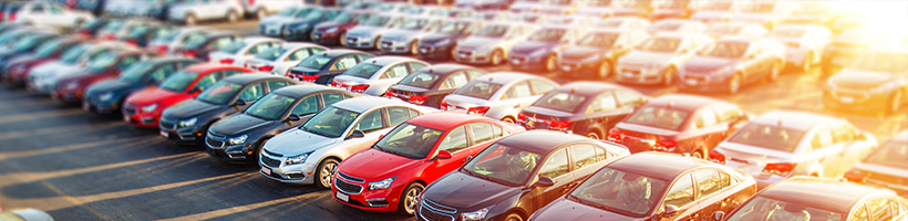 Cars lined up in a parking lot with the sun shining on the cars