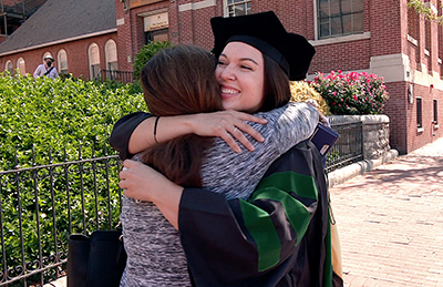 A graduate hugs a family member at a smaller, outdoor commencement celebration