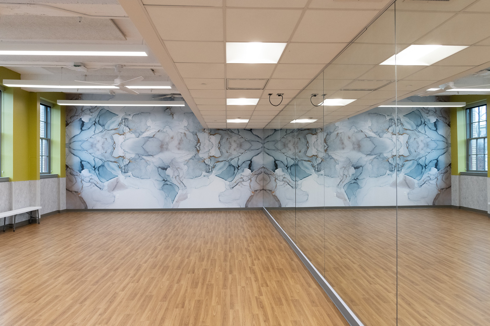 brightly lit fitness room with hardwood floors and a large mirror wall