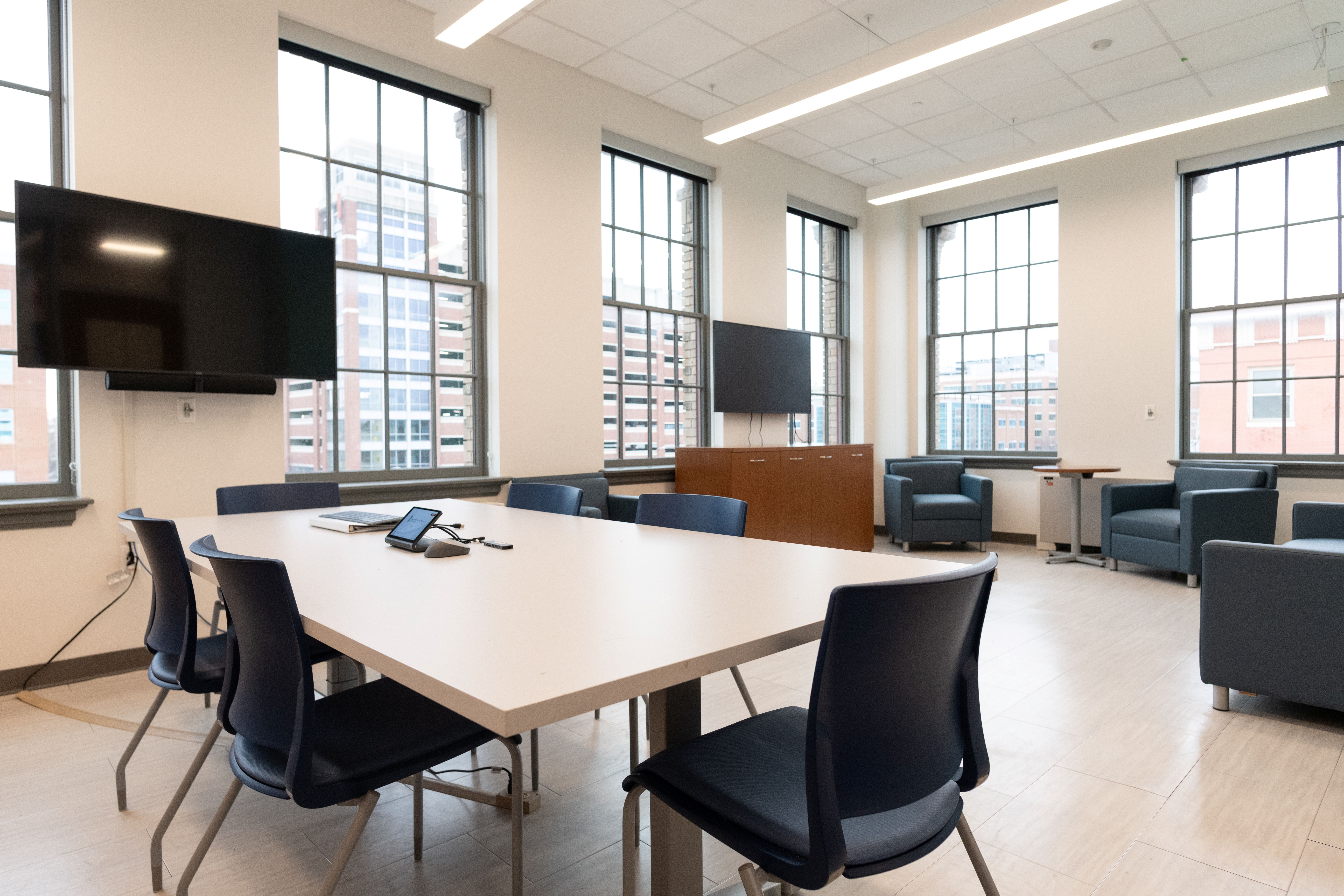 brightly lit room with meeting table, television and club chairs