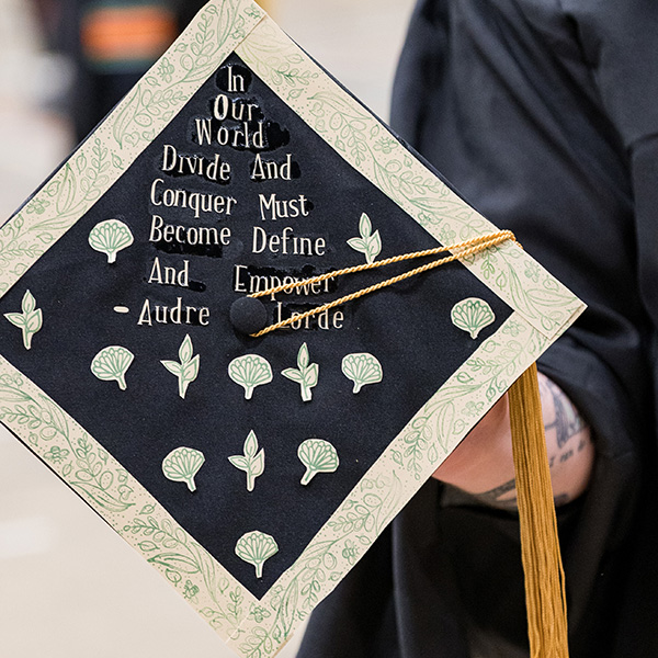 Graduation cap that says In our world, divide and conquer must become define and empower