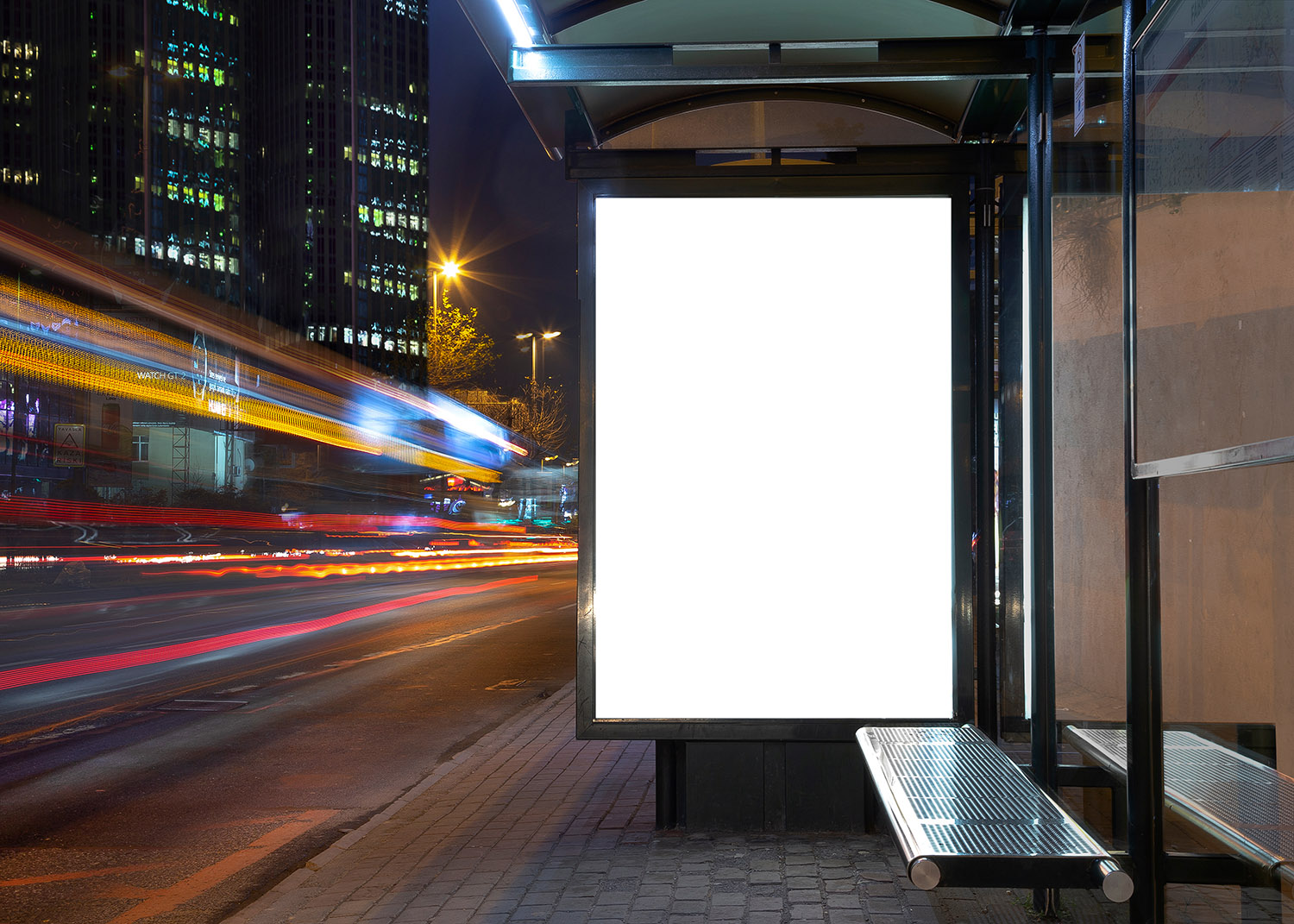 outdoor signage at a bus stop that is blank; city lights in background