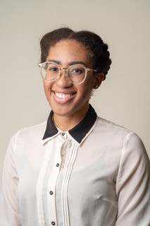 Portrait of Chanelle Hutchinson in a cream button up with a black collar on a beige background
