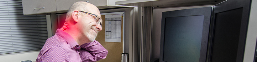 Male in front of computers rubbing his neck away from the pain