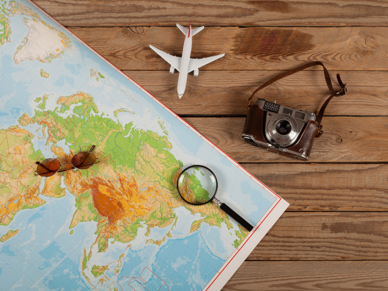 A map with a magnifying glass on a table with a camera and toy airplane
