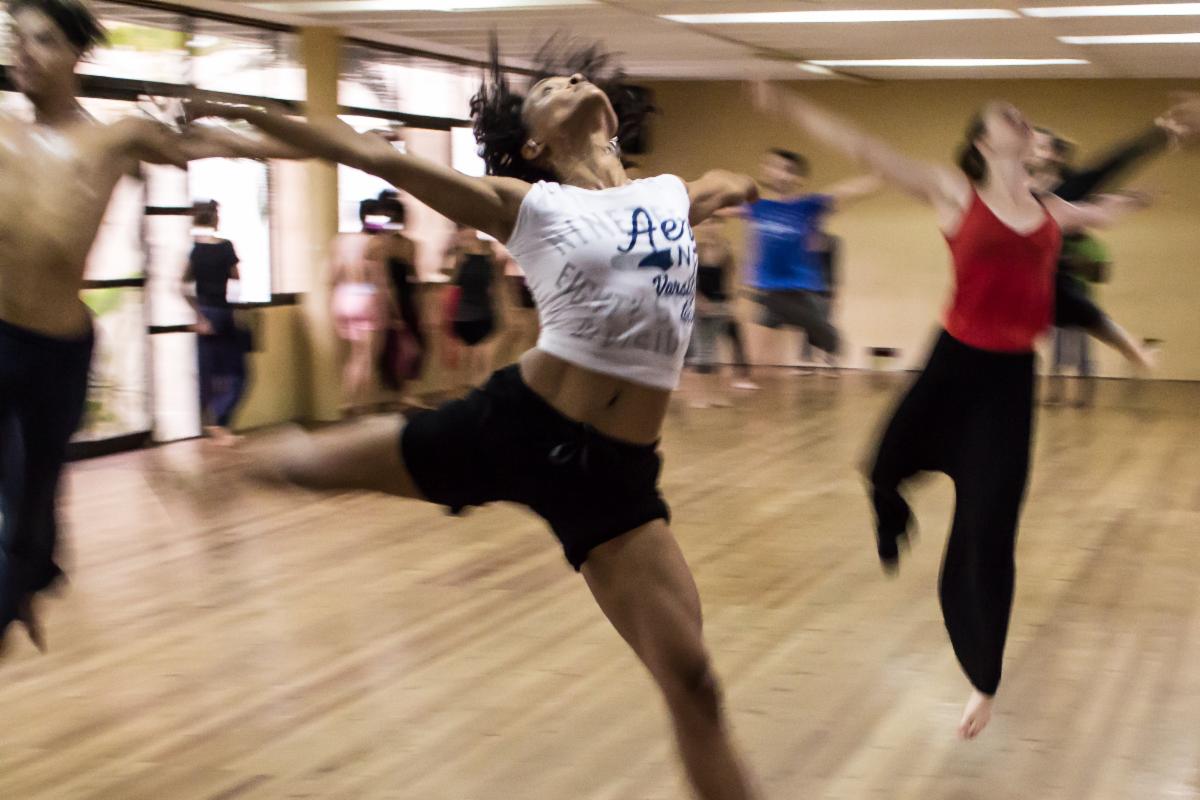 Black woman leaping across dance floor with other dancers in the background
