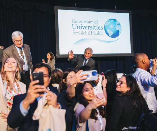 Dr. Fauci stands on a stage behind people taking selfies