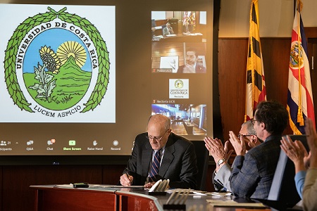 Dr. Bruce Jarrell signs an MOU in front of a screen with video from Costa Rica