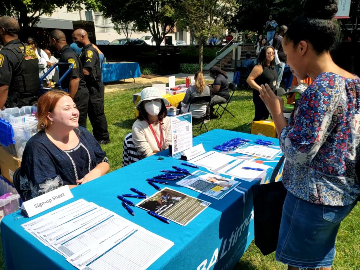 Two staff members sitting behind a table speak to a student at the Fall Kick Off event