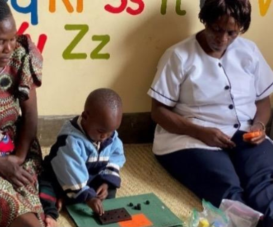 A young boy sits on the floor between his mother and a nurse