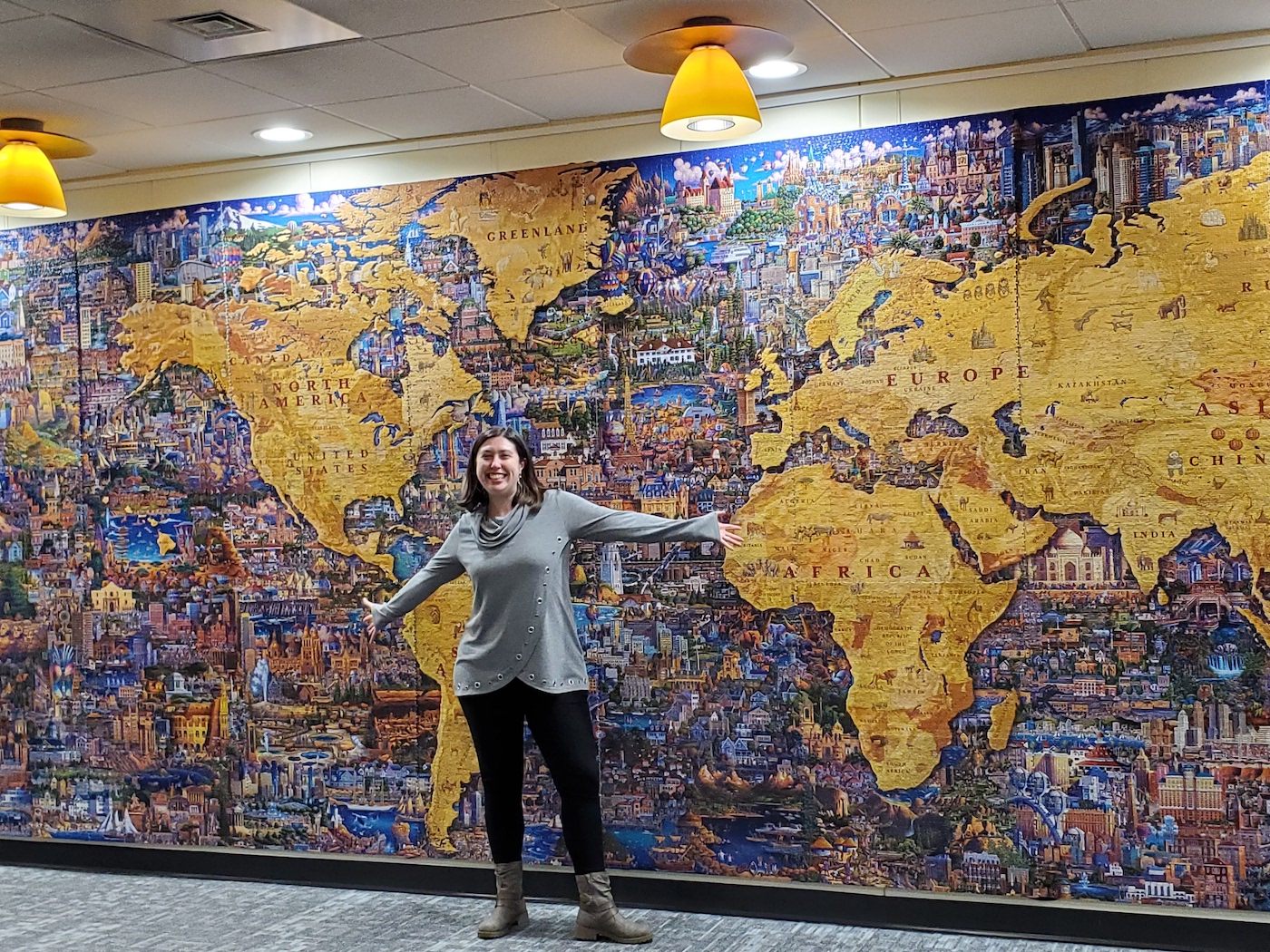 A woman with her arms spread out stands in front of a massive world map puzzle.