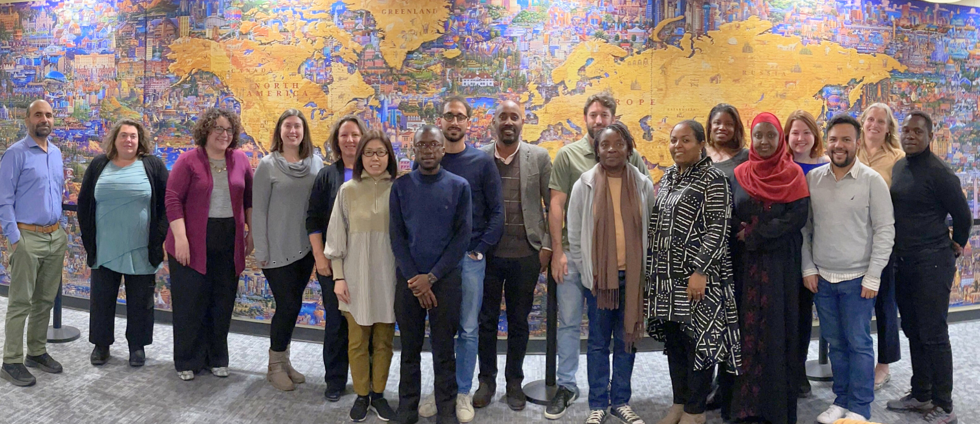 A large group of people pose for a group photo in front of a map.