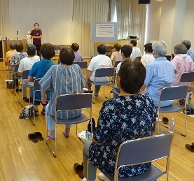 Japanese senior citizens sit in chairs arranged in rows listening to a speaker