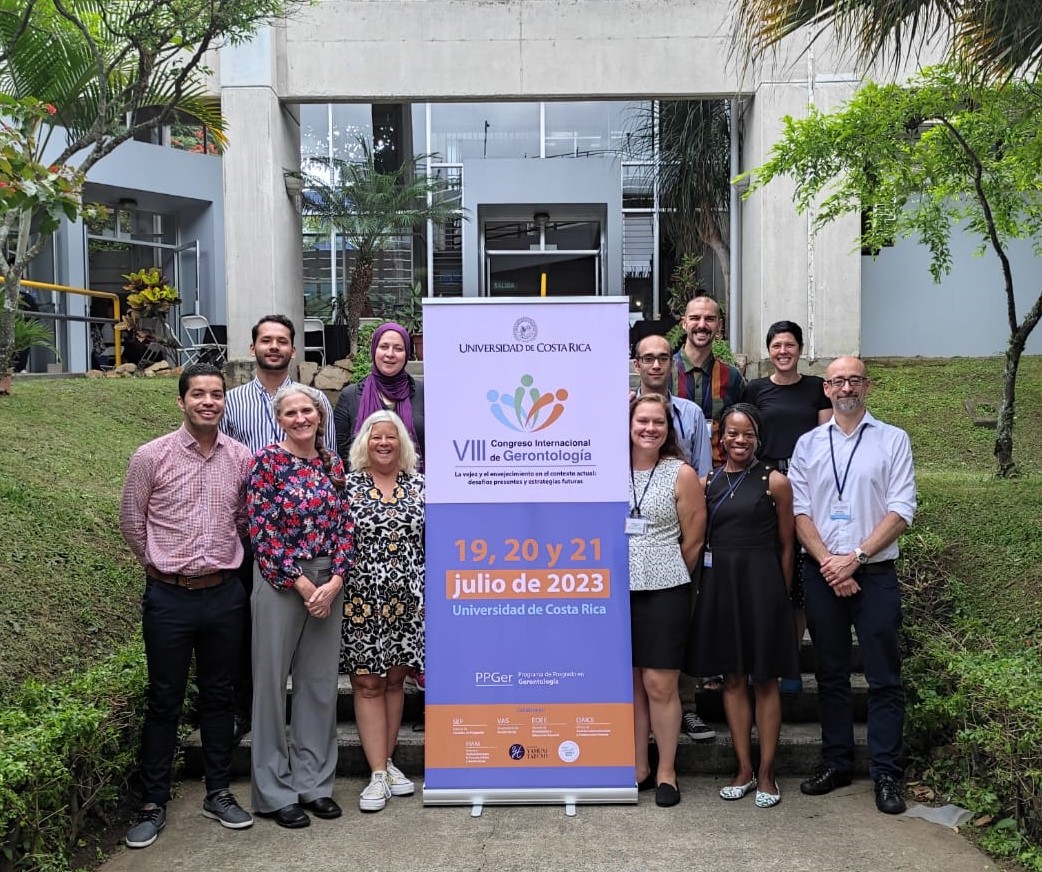 A group of faculty pose for a group photo beside a banner.