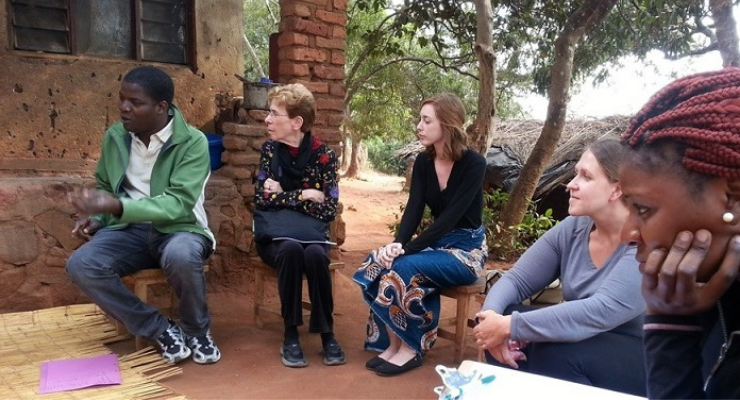 Group of people sitting in a circle outside with trees in background