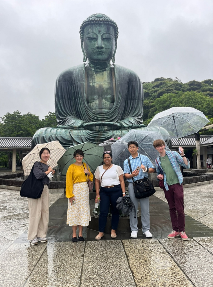 Students and faculty pose under umbrellas in front of a Buddha statue