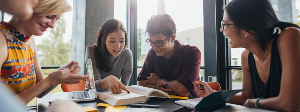 Students look at a book together while sitting at a table