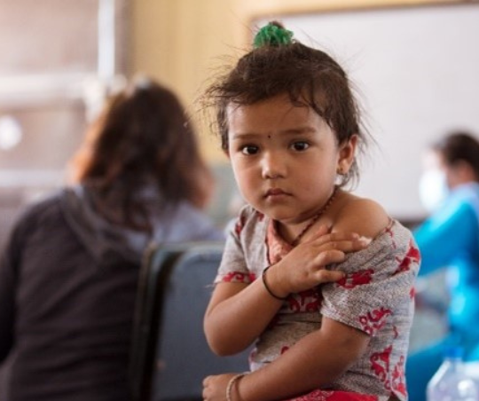 A young child sits holding her upper arm, like she just received a shot