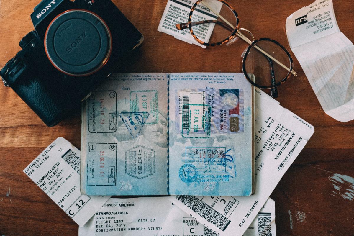 Passport, airline tickets, glasses, and other travel paraphernalia lie on a wood table