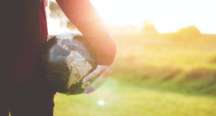 A person's hand holding a globe against their thigh with a sunshiny outdoor background