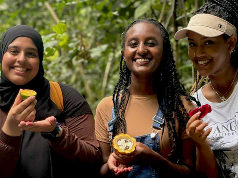 Students holding tropical fruit outside in a forest