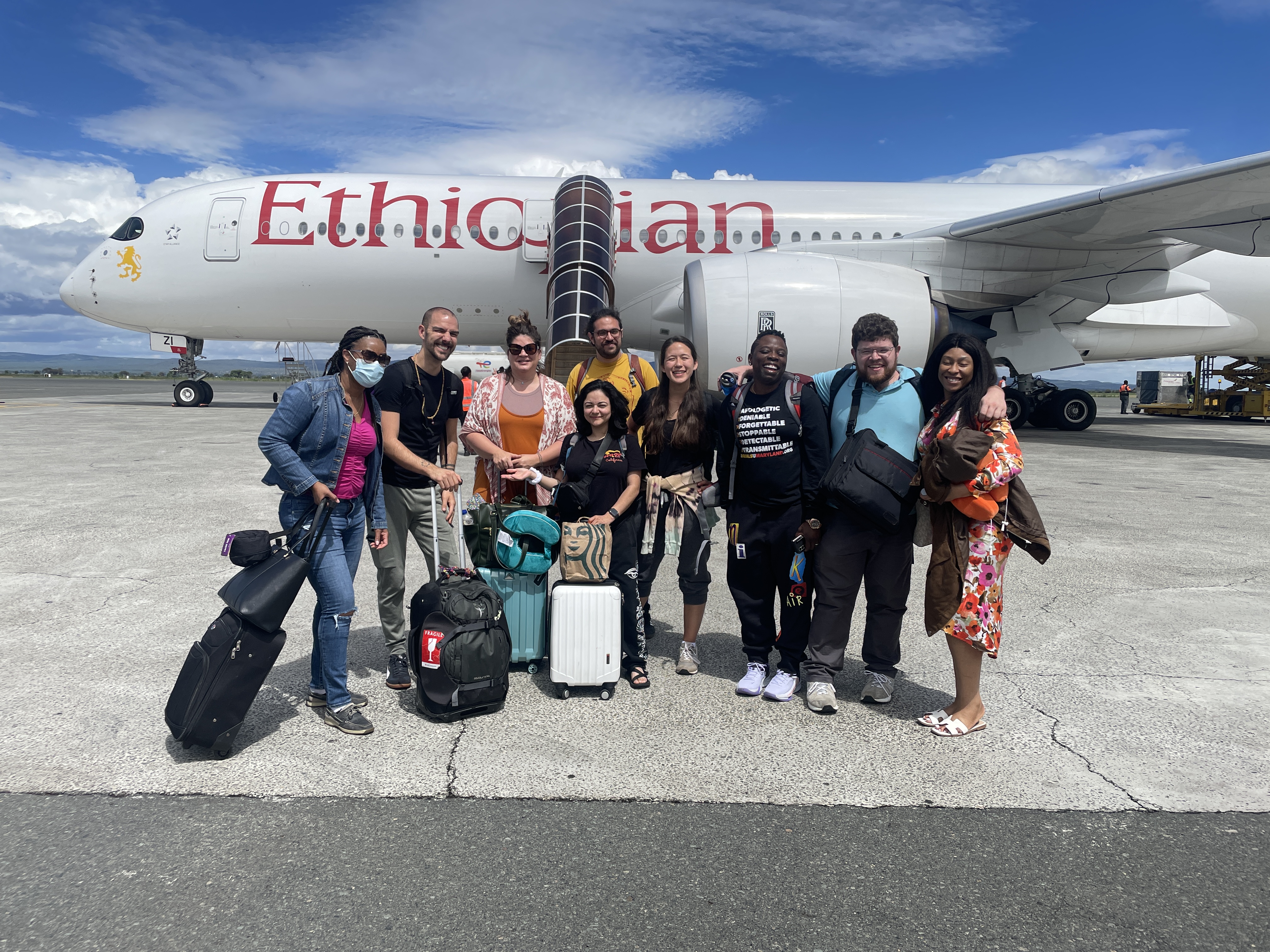 A group of SON faculty and students pose for a group photo in front of an airplane