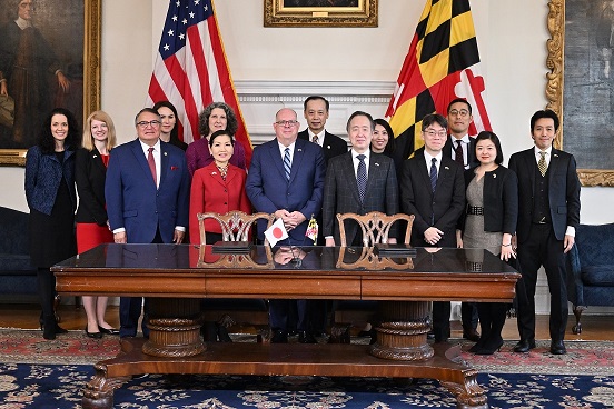 A group of officials from Maryland and Japan pose behind a large table in a ceremonial room