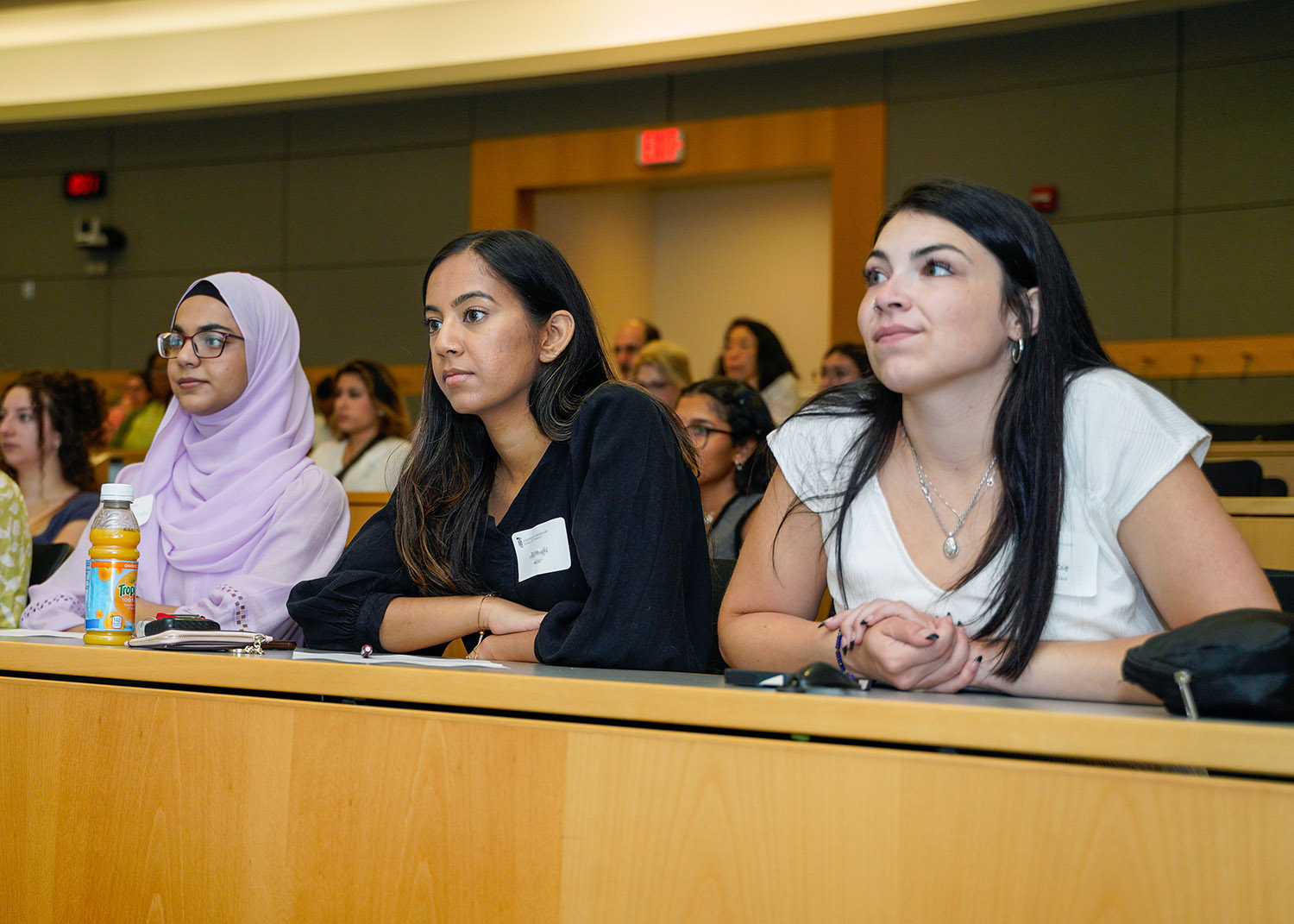 three diverse female presenting students listen during class