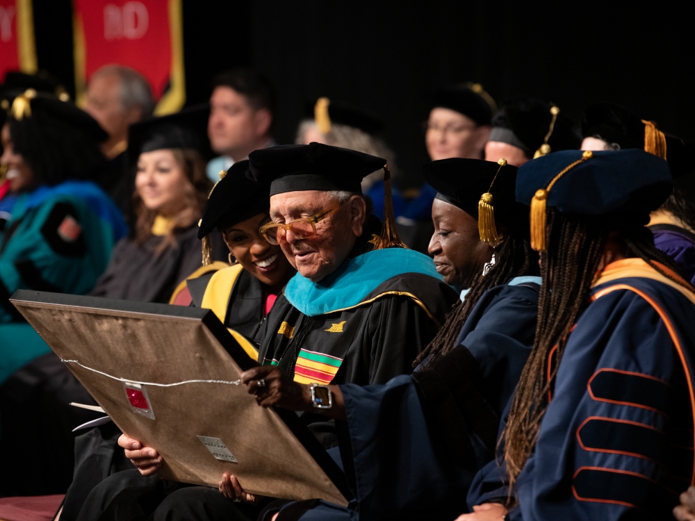 Tisha Edwards, left, and Wendy Shaia, right, admire the framed honorary UMB Doctor of Public Service held by Ronald Chisom.