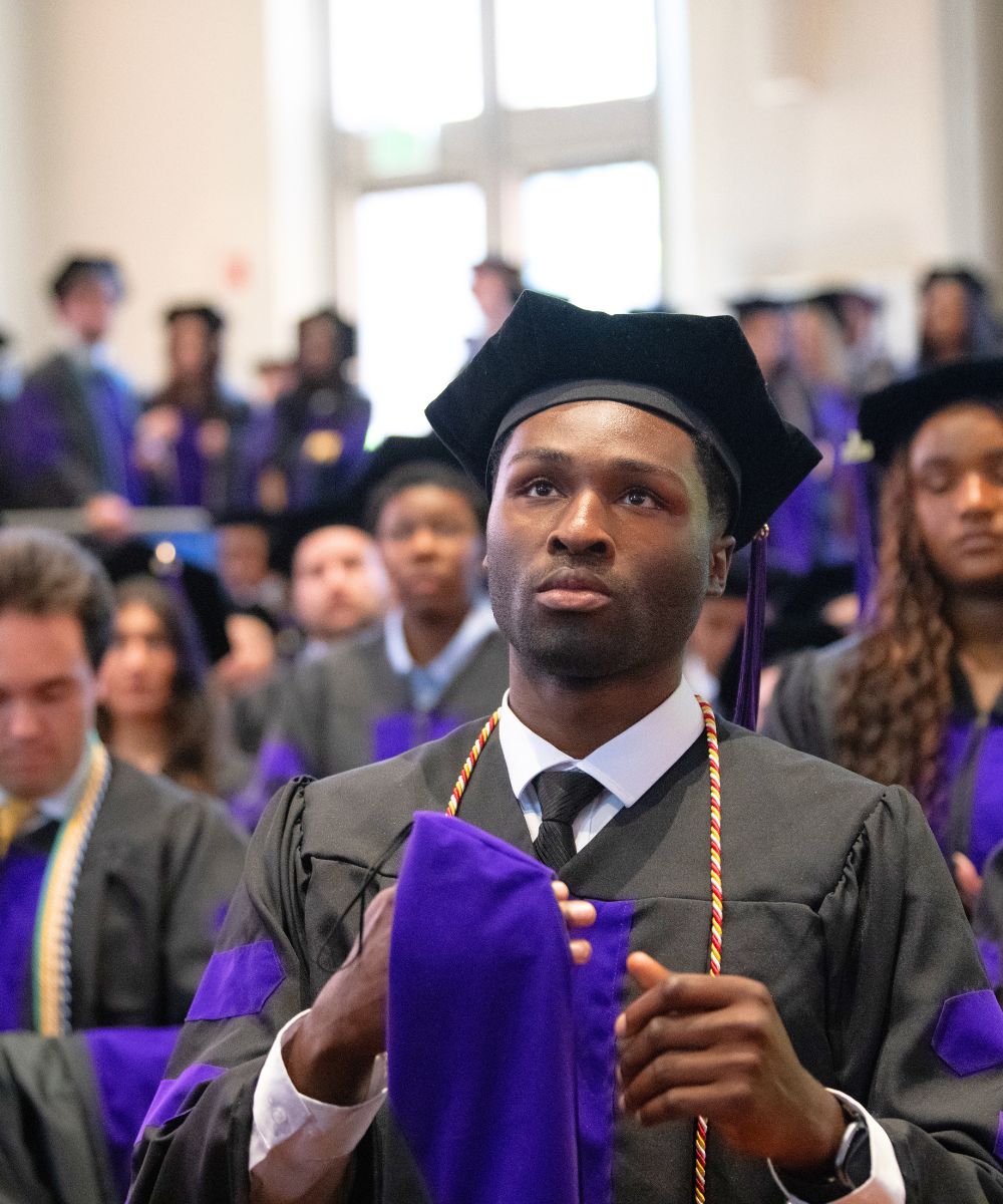 A law student in cap and gown looks pensive