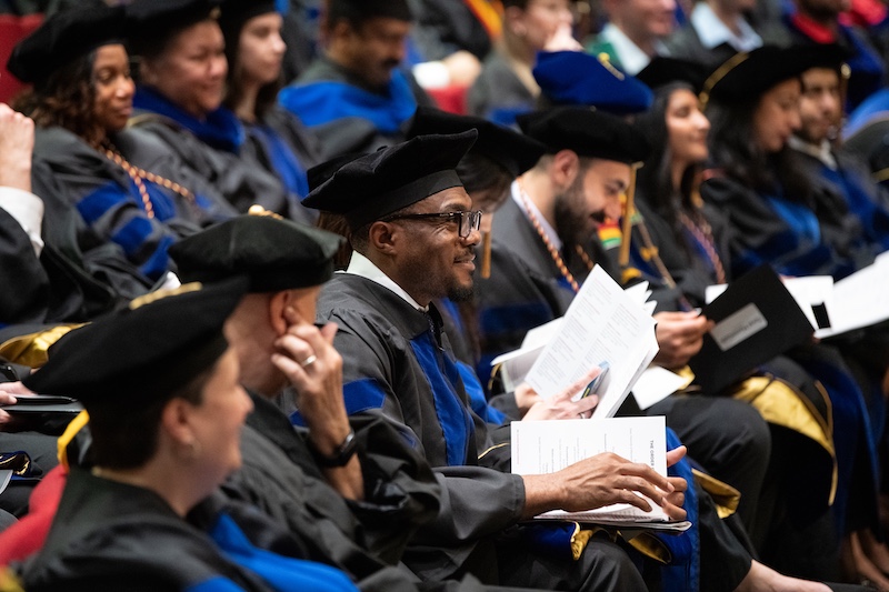 Doctoral candidates sit in Leadership Hall during the University of Maryland, Baltimore’s 2026 Doctoral Hooding Ceremony, watching as graduates are recognized and hooded on stage.