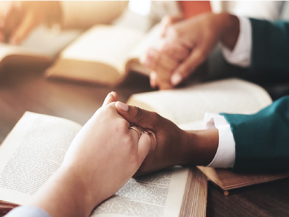 Two people holding hands while in prayer.