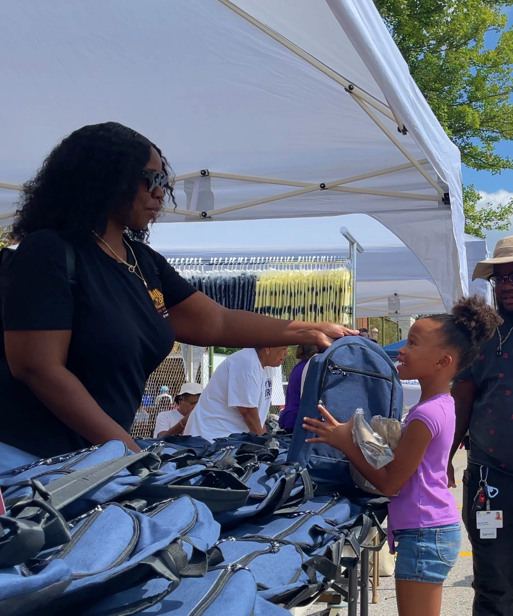 Young girl receiving a free blue backpack from an adult at the Back to School Bash