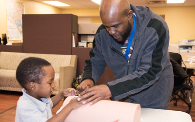 Alan Brown helps Blair Pinacle, 5, learn how to stop a wound from bleeding at UMB's Community Engagement Center.