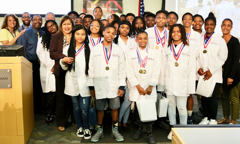 Sanya Springfield, PhD, director of the Center to Reduce Cancer Health Disparities, in the second row, left, stands with eighth-graders in the UMB CURE Scholars Program who are anticipating their selective high school placements. They were among 80 scholars honored for 2017-18 accomplishments on May 5 by leaders including executive director Robin Saunders, EdD, MS, back row, far left.

